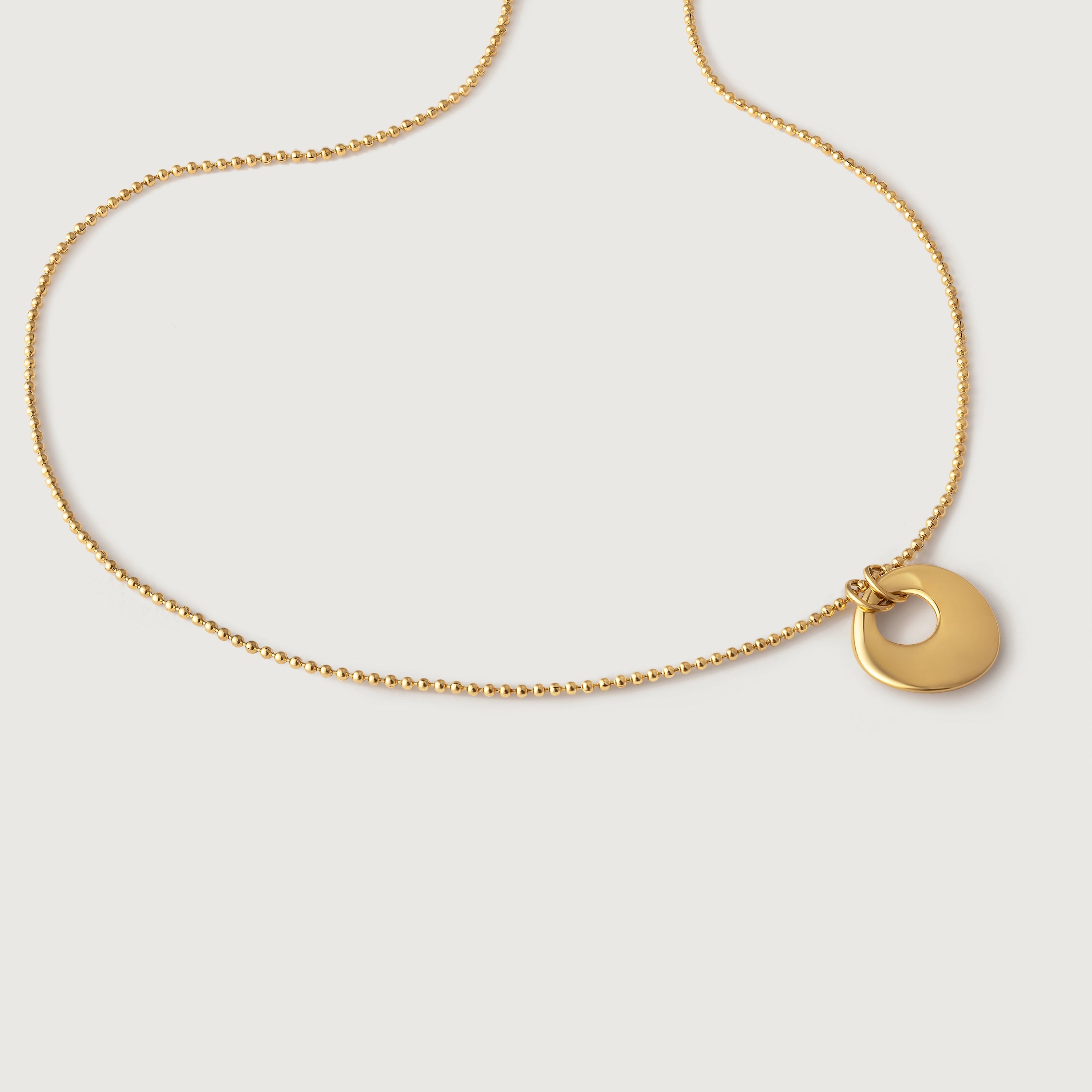 A gold-plated necklace with a simple circular charm and a textured chain.
