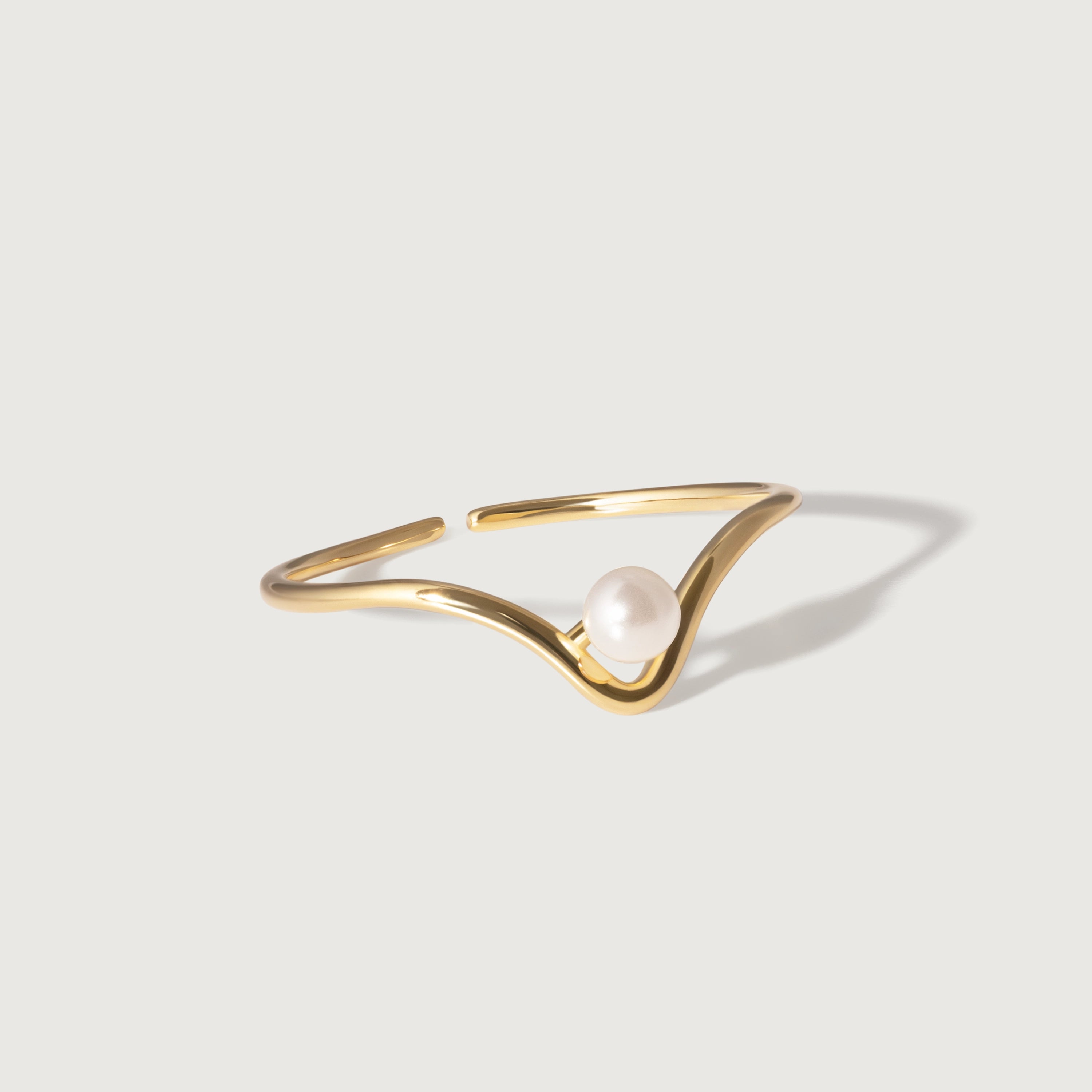A gold-plated ring with a wave-like design featuring a lustrous pearl at the crest, on a white background.