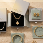 Jewelry set including necklace, bracelet, and earrings in Kaleya boxes on a beige surface.