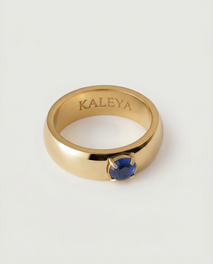 A gold-colored ring with a blue cubic zirconia gemstone in the center, displayed against a white background.