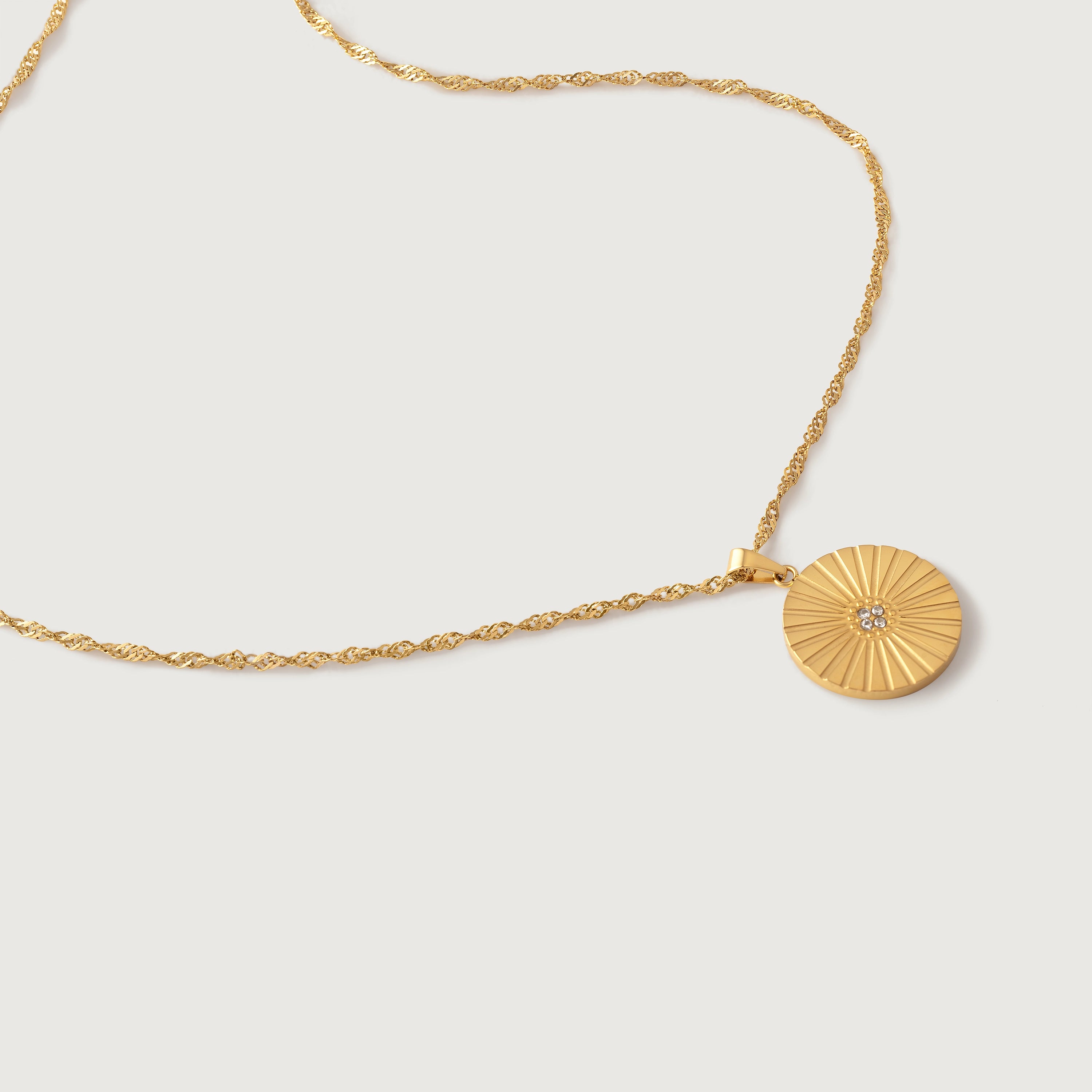A gold-colored necklace with a radially textured medallion pendant hanging from a twisted rope chain.