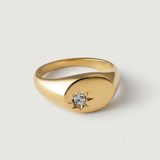 A gold-plated signet ring with an oval face featuring a dazzling stone set in a starburst pattern.