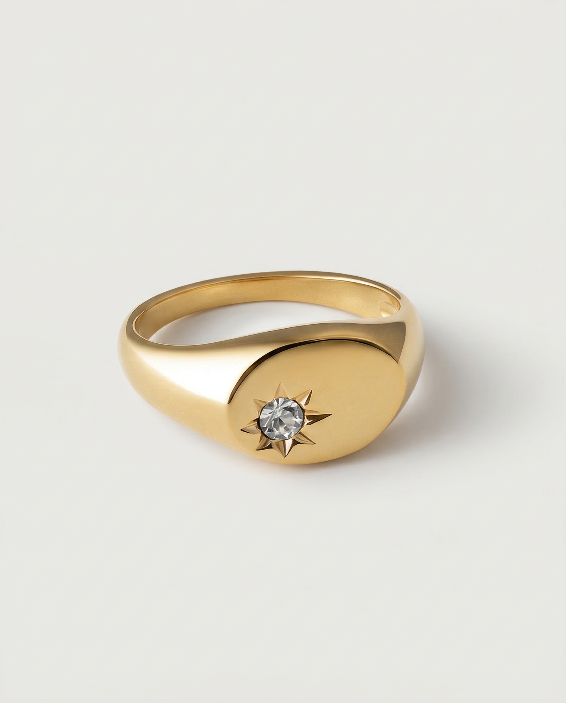 A gold-plated signet ring with an oval face featuring a dazzling stone set in a starburst pattern.