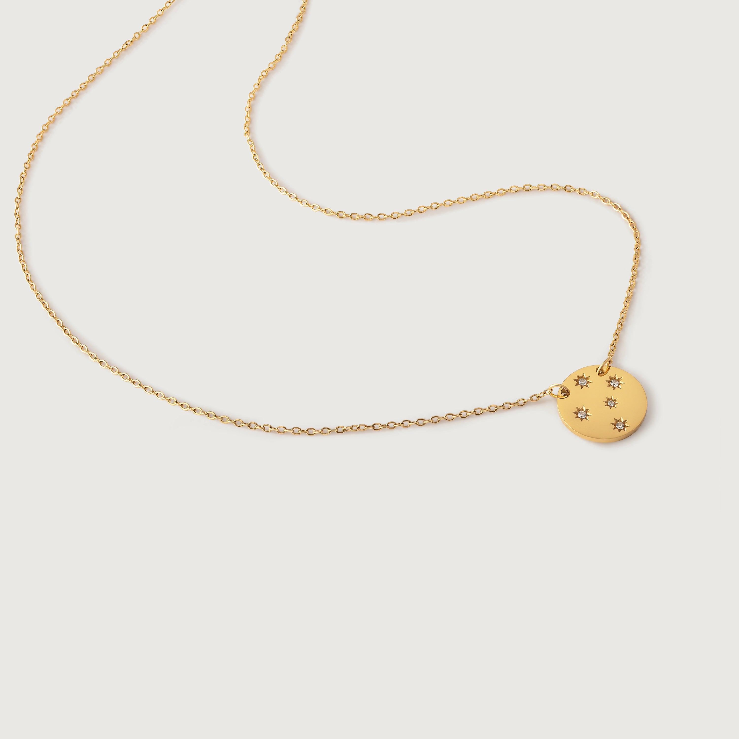 A gold-plated necklace with a round medallion pendant adorned with crystal stars on a brushed metal disc, displayed against a white background.