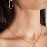 model wearing a gold-colored necklace with a radially textured medallion pendant hanging from a twisted rope chain.