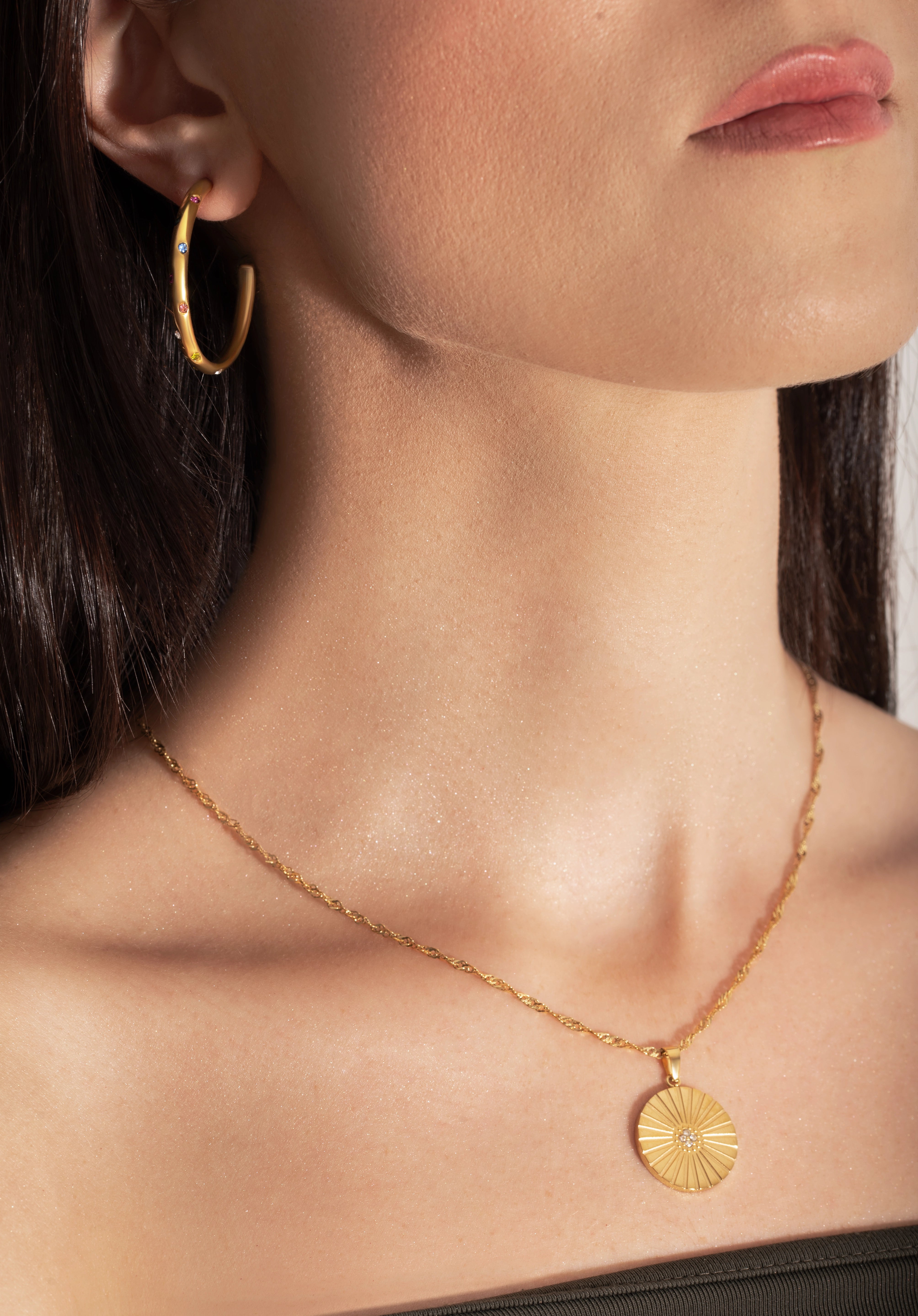 model wearing a gold-colored necklace with a radially textured medallion pendant hanging from a twisted rope chain.