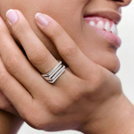 Close-up of a hand wearing a silver ring with a bold, architectural design consisting of layered silver plates.