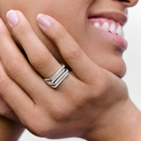 Close-up of a hand wearing a silver ring with a bold, architectural design consisting of layered silver plates.