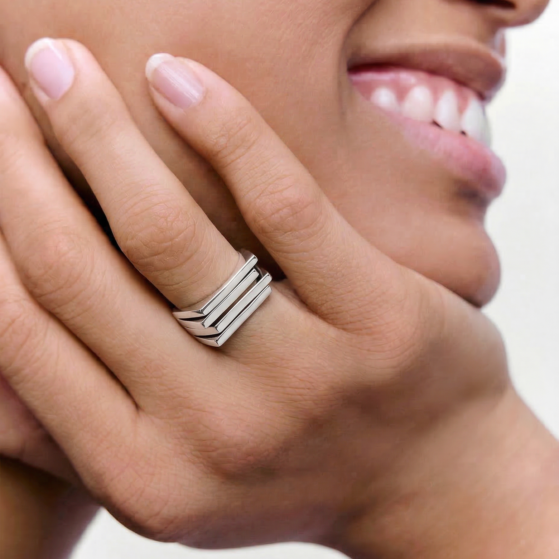 Close-up of a hand wearing a silver ring with a bold, architectural design consisting of layered silver plates.