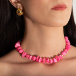 a close up photo of a model wearing a pink coral nuggets necklace with metallic beads and a gold heart charm