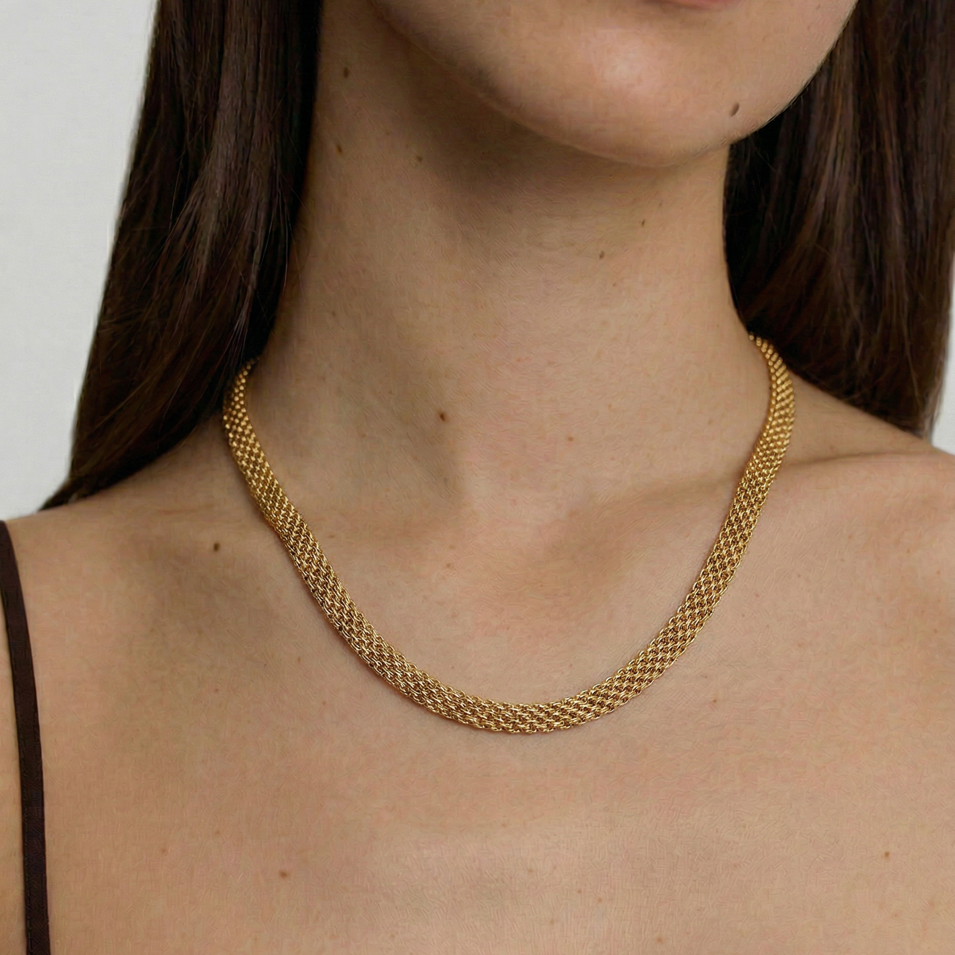 model wearing a gold-plated mesh necklace with a fluid ribbon design