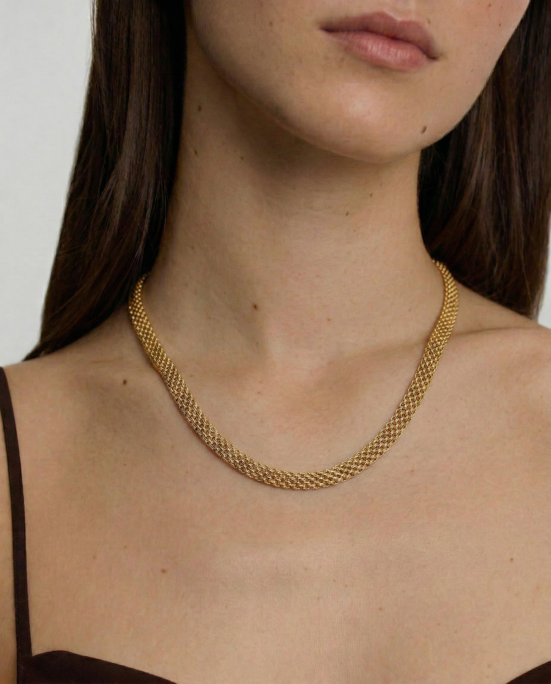 model wearing a gold-plated mesh necklace with a fluid ribbon design