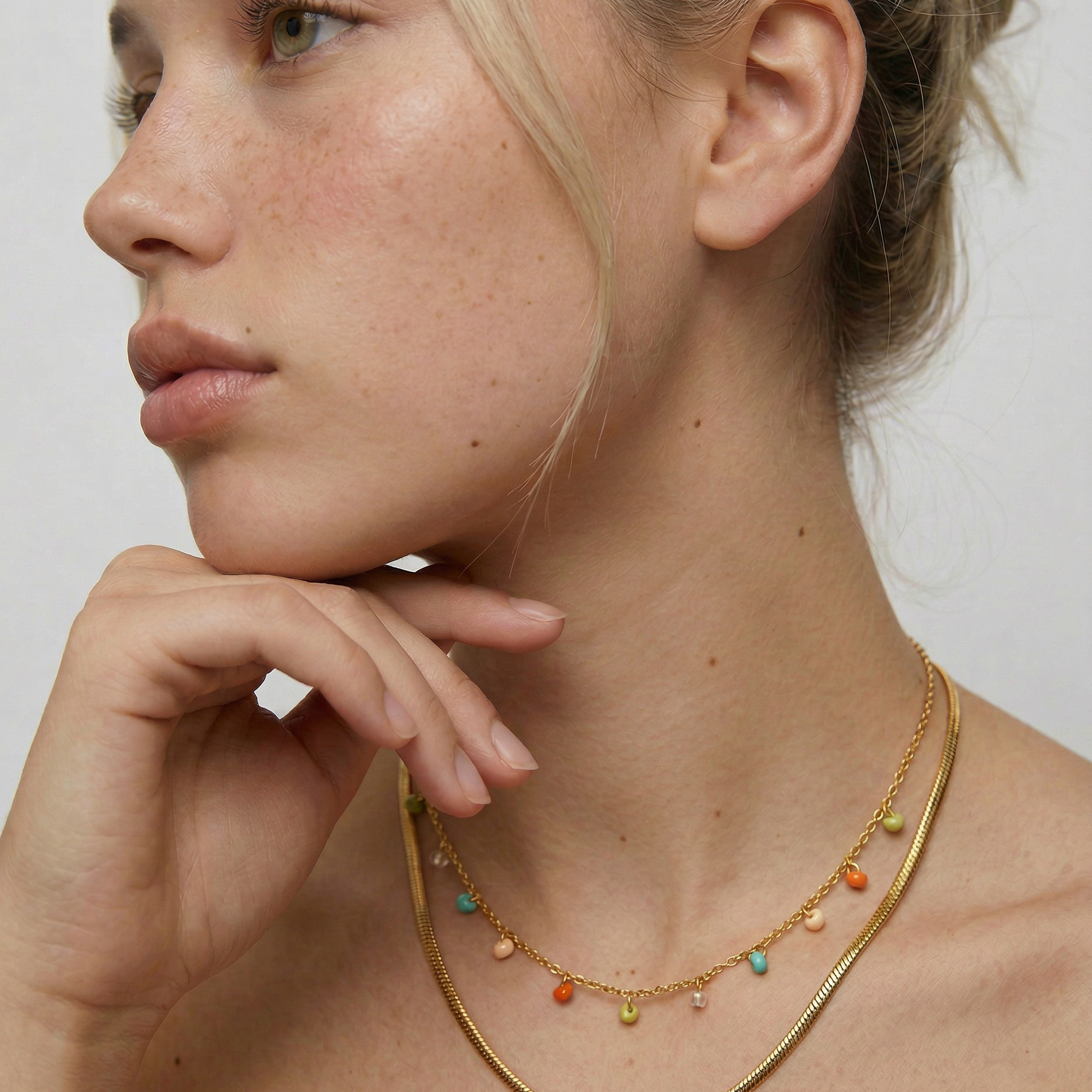 Woman wearing a gold necklace with colorful beads against a neutral background
