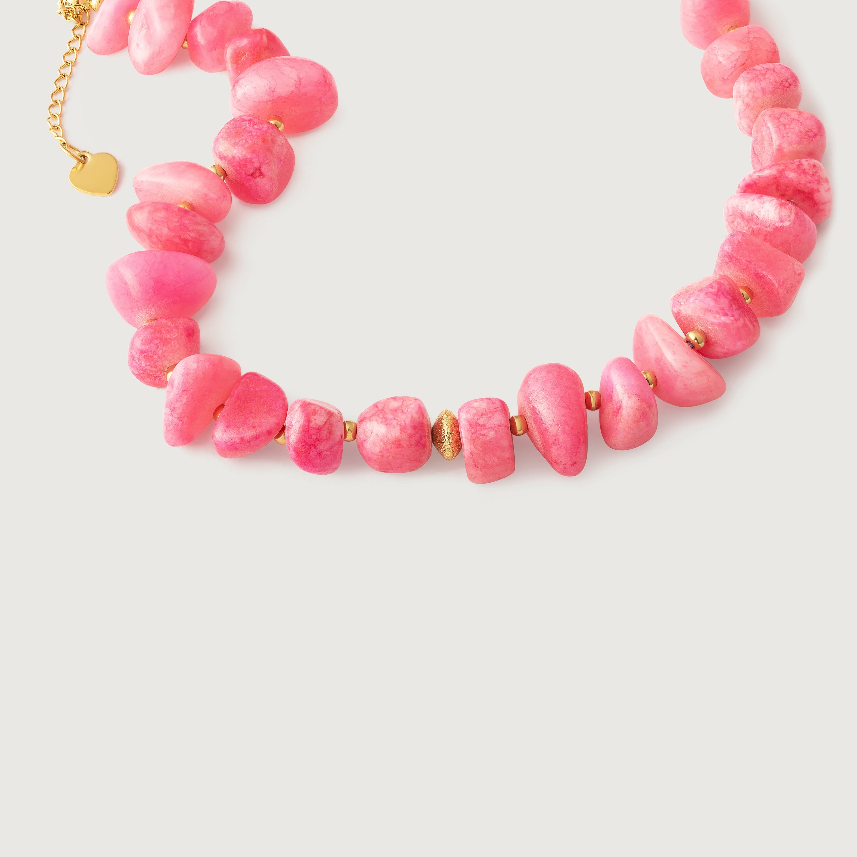 A pink coral nuggets necklace with metallic beads and a gold heart charm, displayed against a white background.