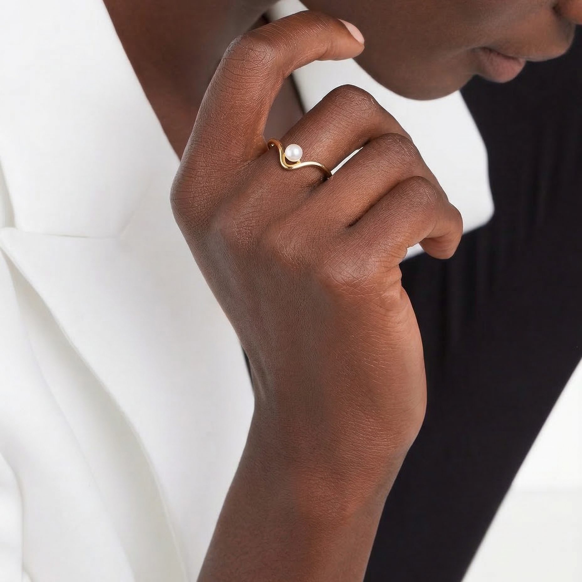 Close-up of a hand wearing a gold ring with a white stone on a neutral background