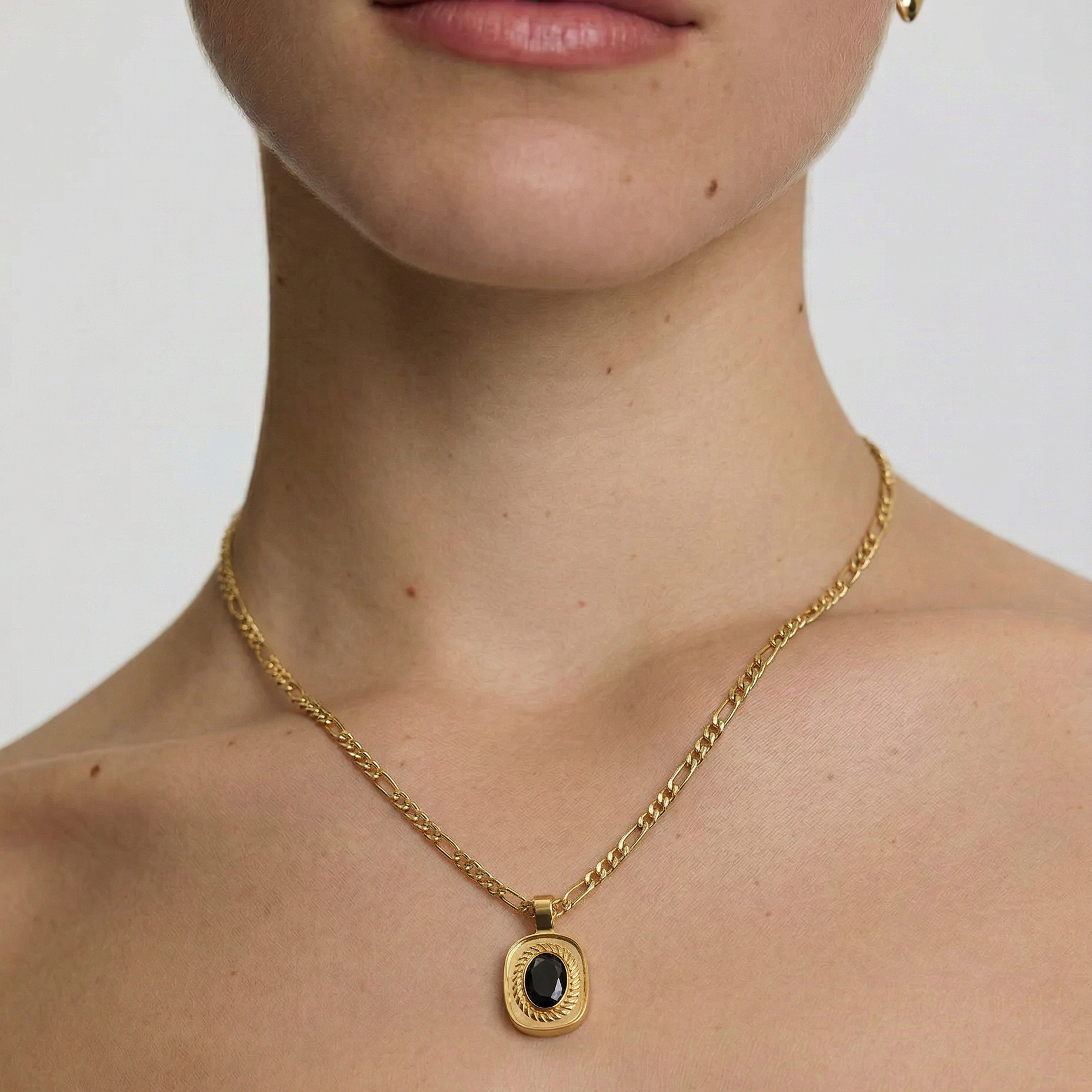 Close-up of a person wearing a gold necklace with a black pendant on a plain background
