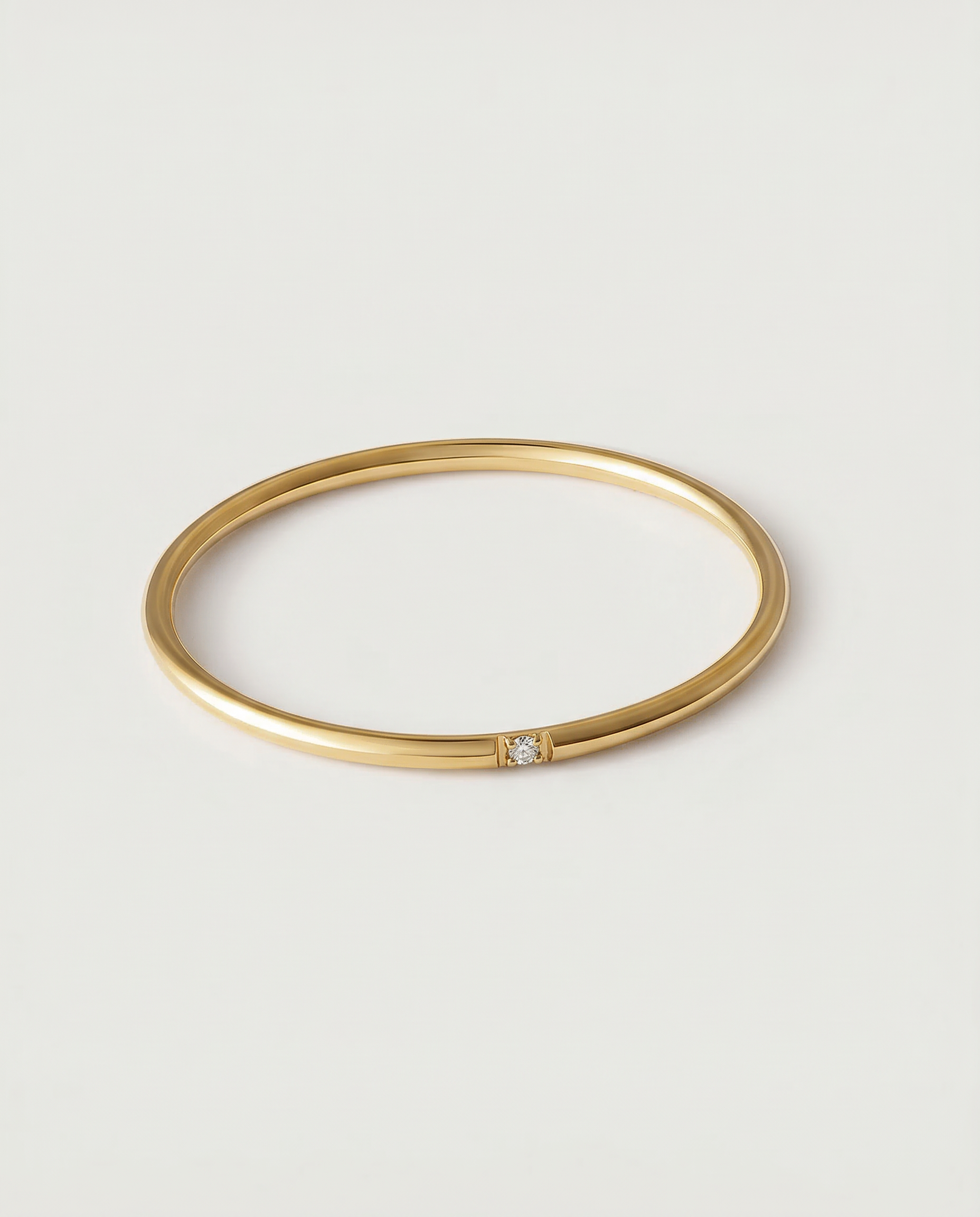 A gold-colored band ring with a single sparkling stone on a white background.