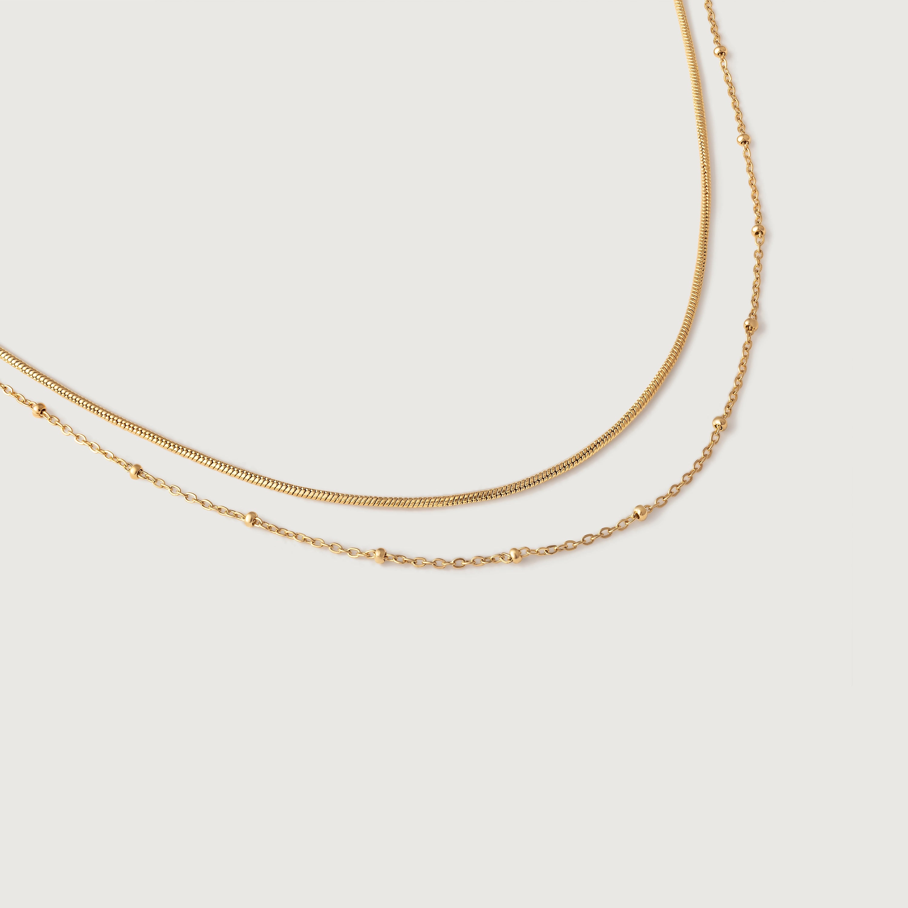 A layered choker necklace with one sleek snake chain and another with tiny spherical stations, both in 18k gold plating.