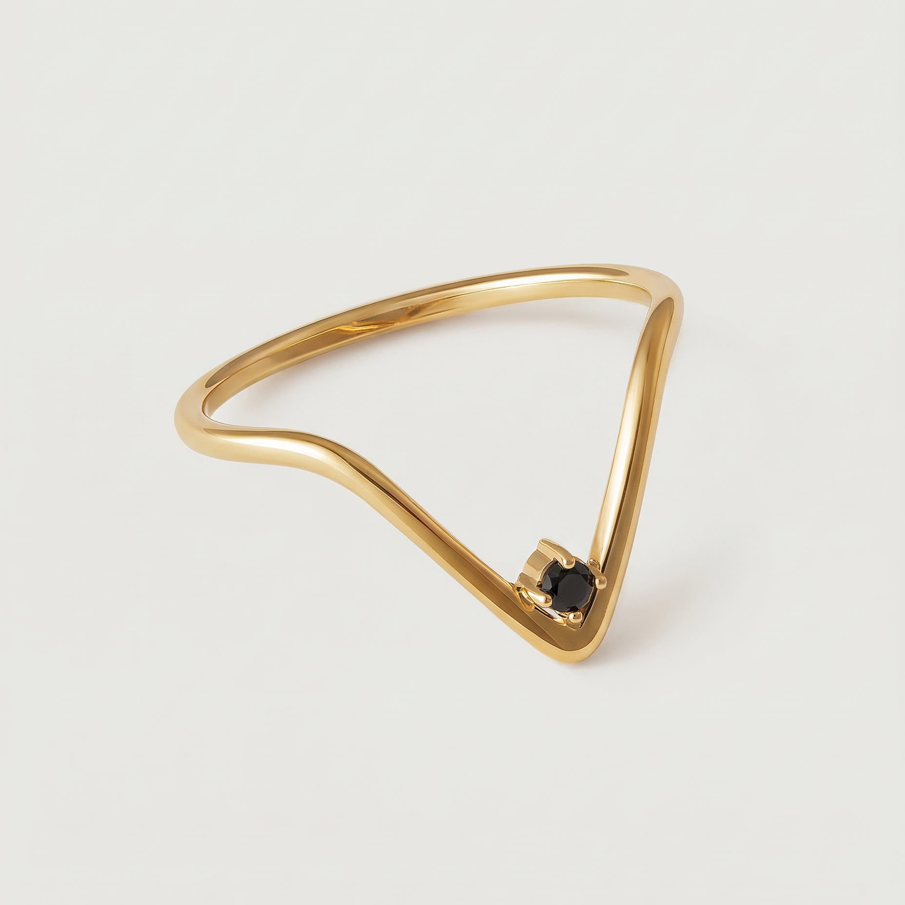 A gold-plated ring with an angular design and a black crystal set in a V-formation on a white background.