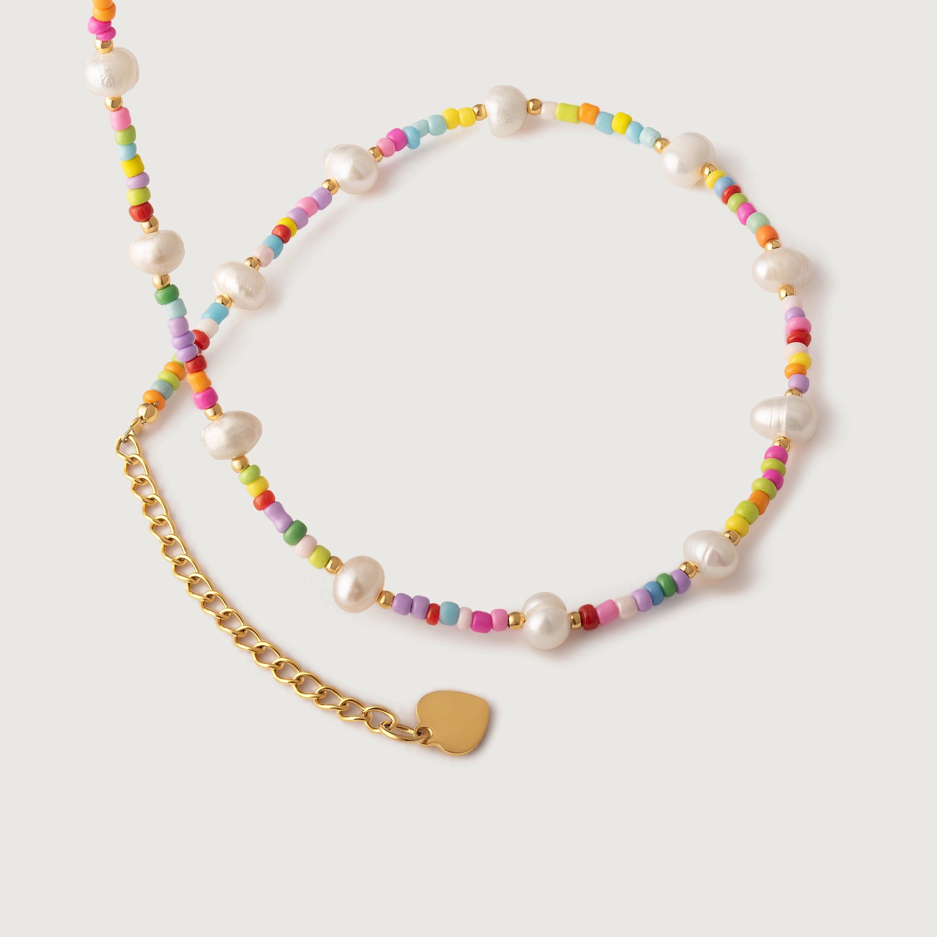 A colorful necklace with white freshwater pearls and multicolored beads, featuring a gold-colored chain and a heart charm.