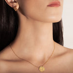 studio model wearing a gold-plated necklace with a round medallion pendant