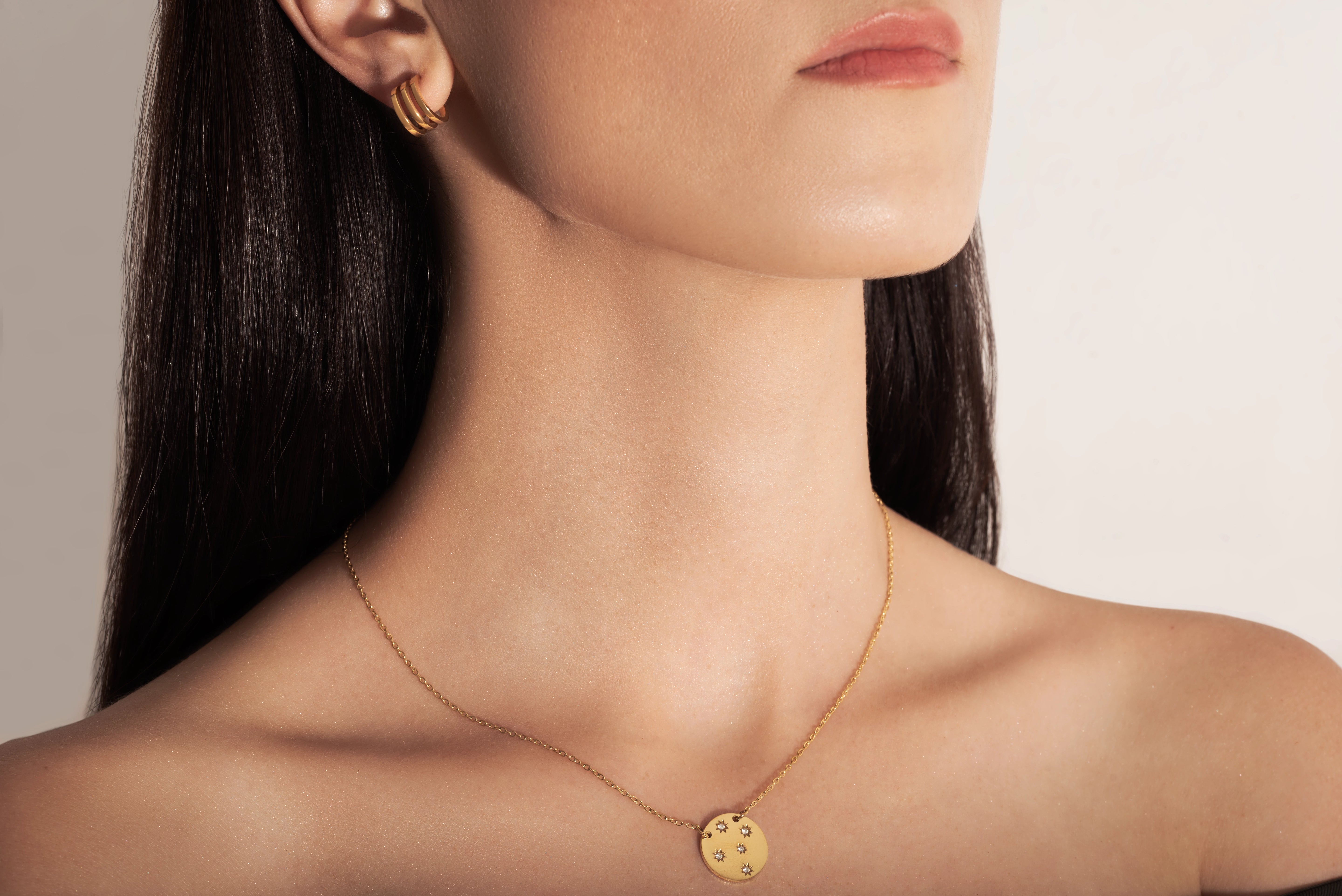studio model wearing a gold-plated necklace with a round medallion pendant