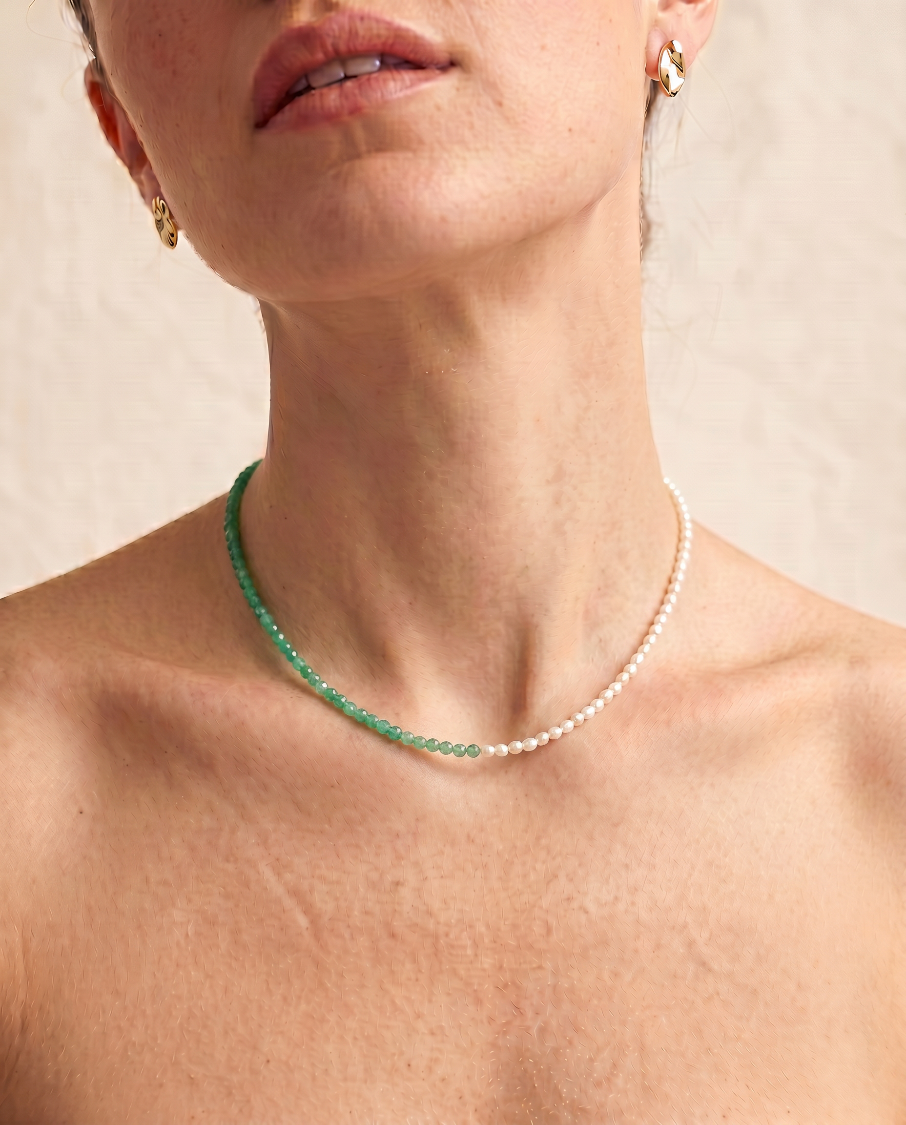 close up of a female model wearing a green aventurine and pearl beaded necklace in gold, with one half strung with pearls and the other half with faceted green aventurine beads in fresh green tones.