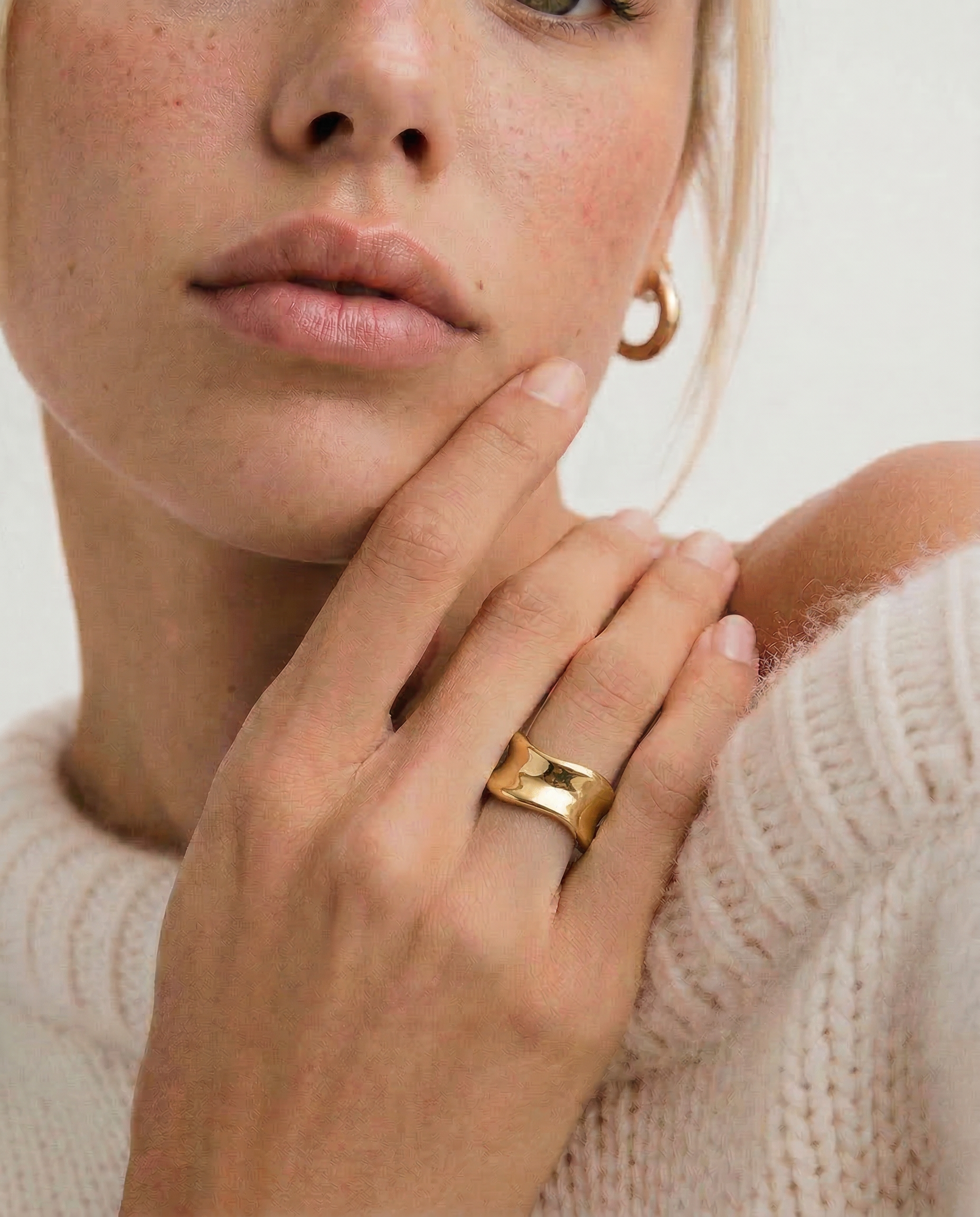 Woman wearing a gold ring on her finger with a neutral background