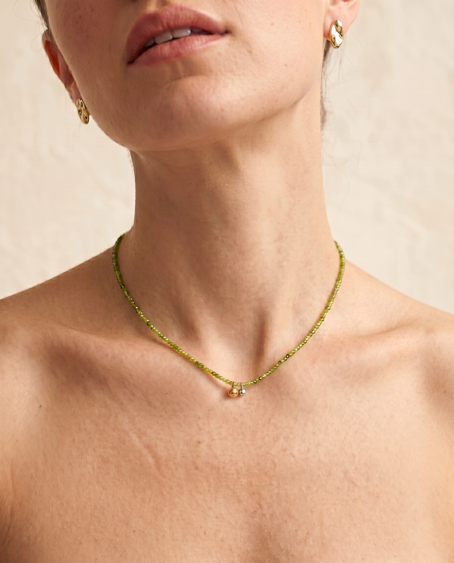 Model wearing the Olive green beaded necklace, the faceted green strand sitting close to the collarbone with the gold and silver ball pendants resting at the centre-front.