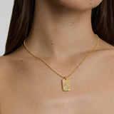 Gold necklace with a rectangular pendant worn by a person