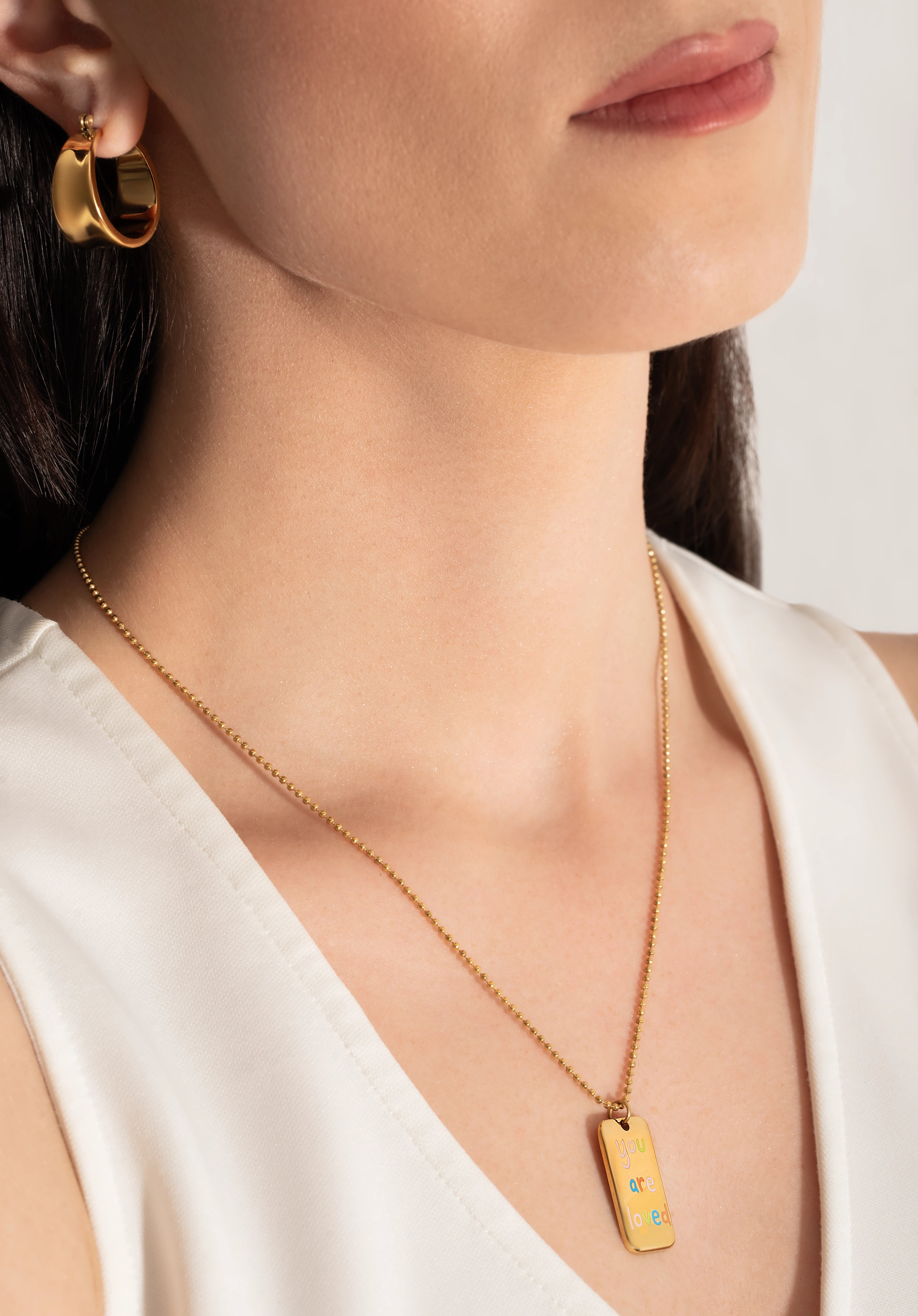 close up of a model wearing a gold-plated necklace with a pendant featuring the phrase 'you are loved' 