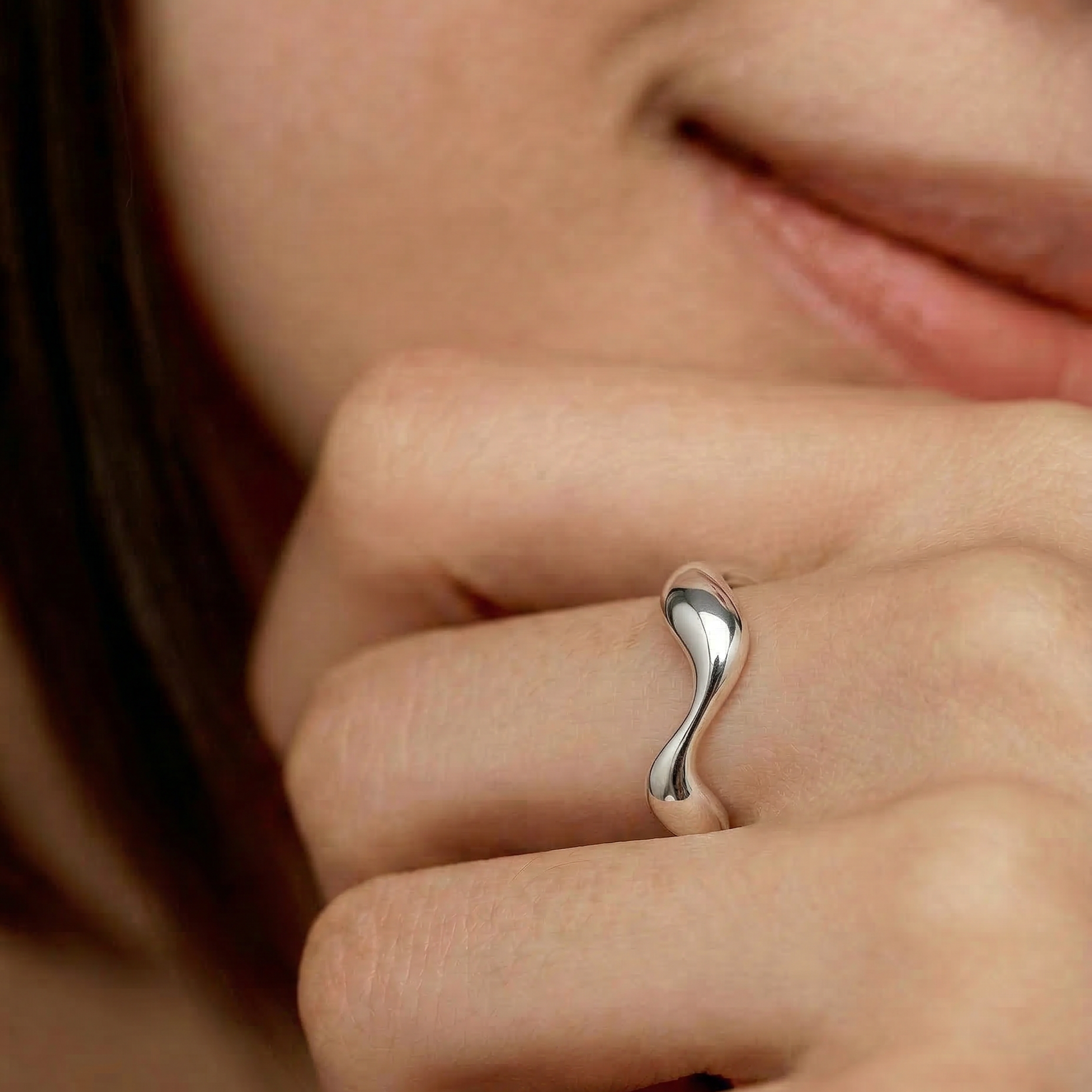 close up of a female model wearing a sleek silver ring with an undulating design, crafted from sterling silver