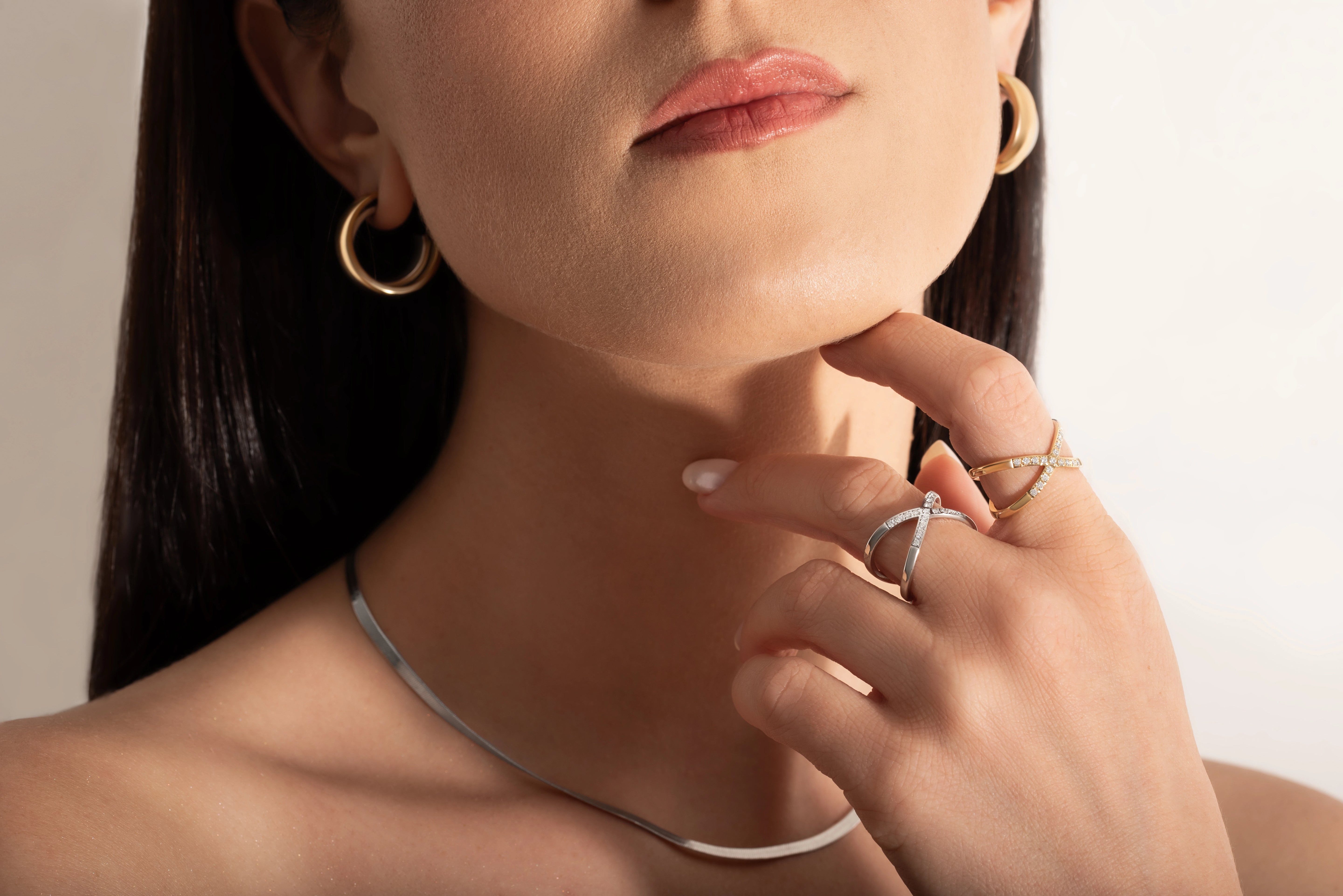close up of a model wearing two gold and silver rings with two intersecting bands and small stones set along one band