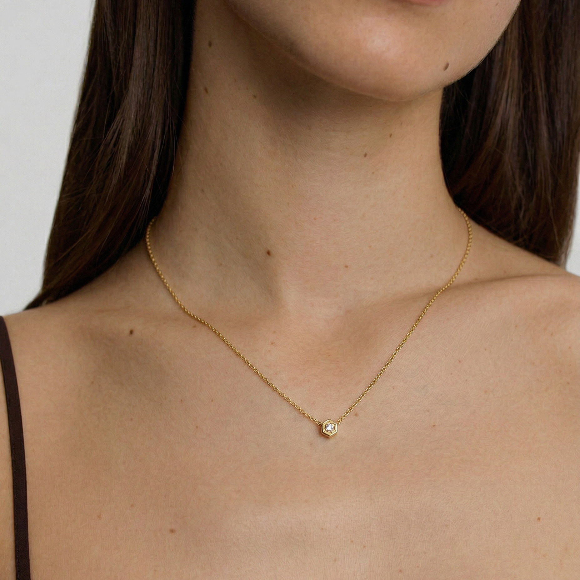 female model wearing a gold necklace with a small round pendant 