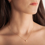 model wearing a delicate gold-plated necklace with a hexagonal setting and a single crystal pendant.