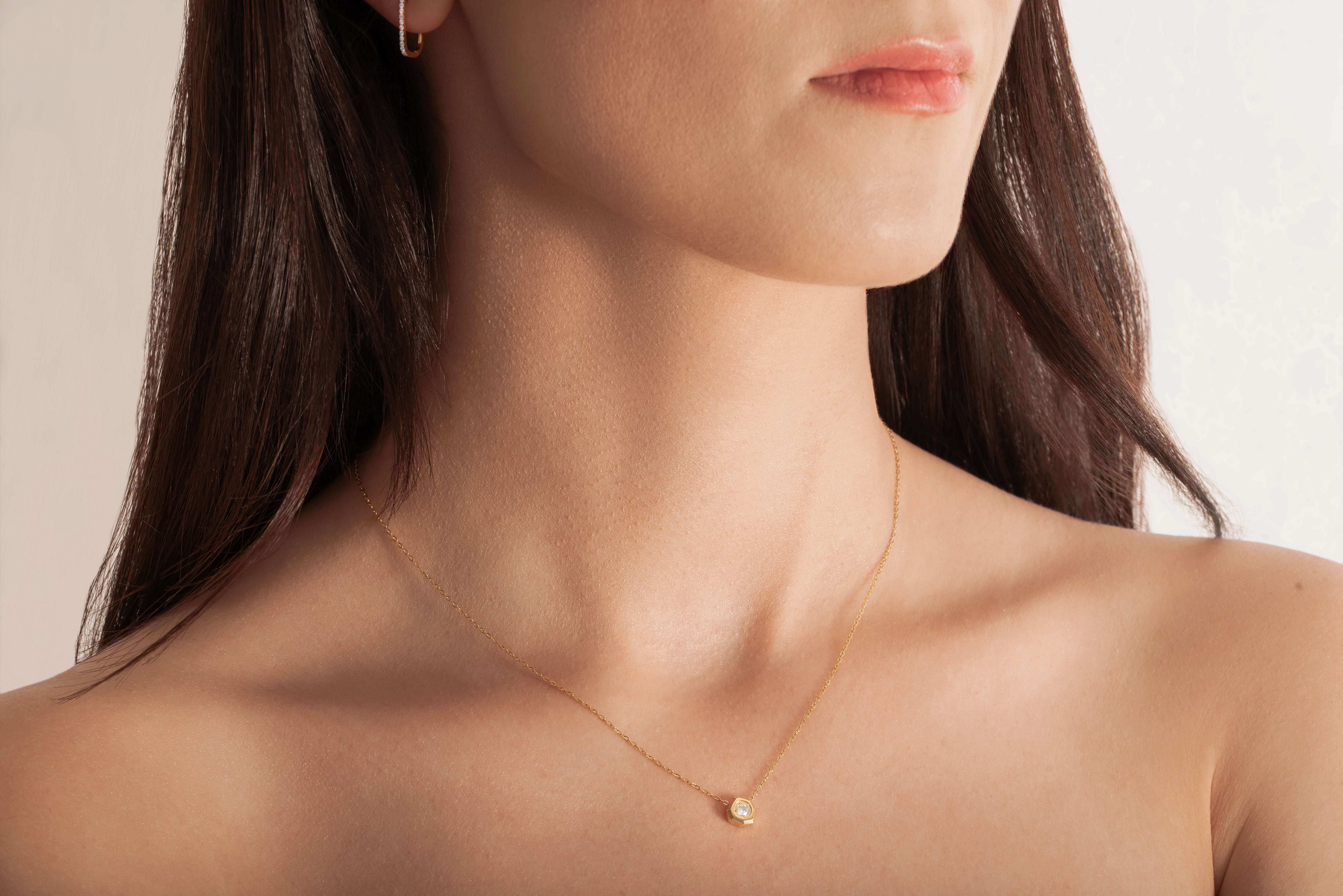 model wearing a delicate gold-plated necklace with a hexagonal setting and a single crystal pendant.