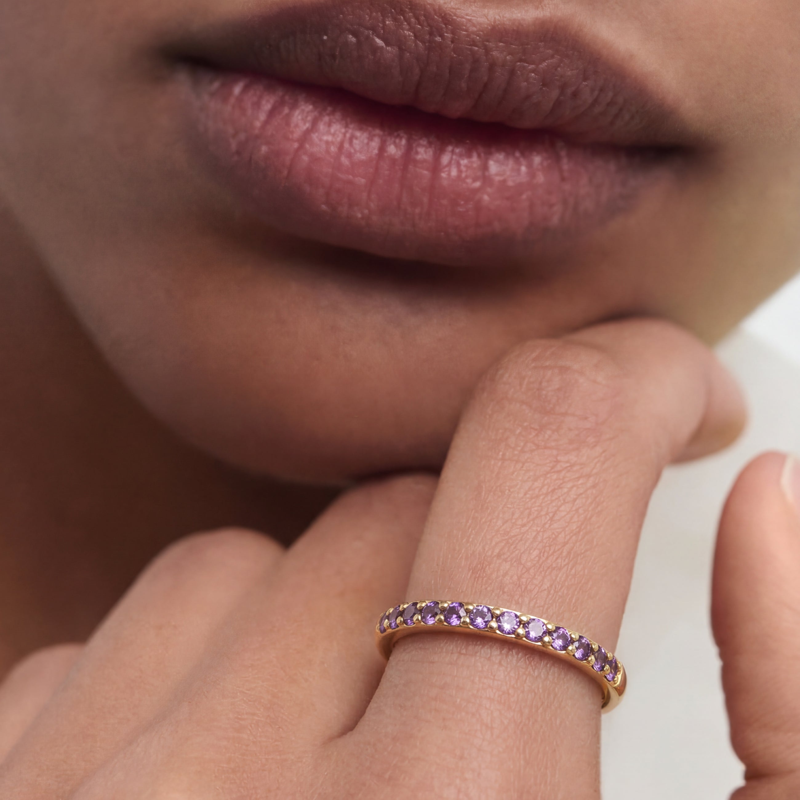 Close-up of a hand wearing a rose gold ring with purple gemstones, resting on a blurred background.