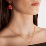 close up of a model wearing a gold-colored necklace with two layers, featuring tiny spheres on the upper strand and a crystal pendant on the lower chain