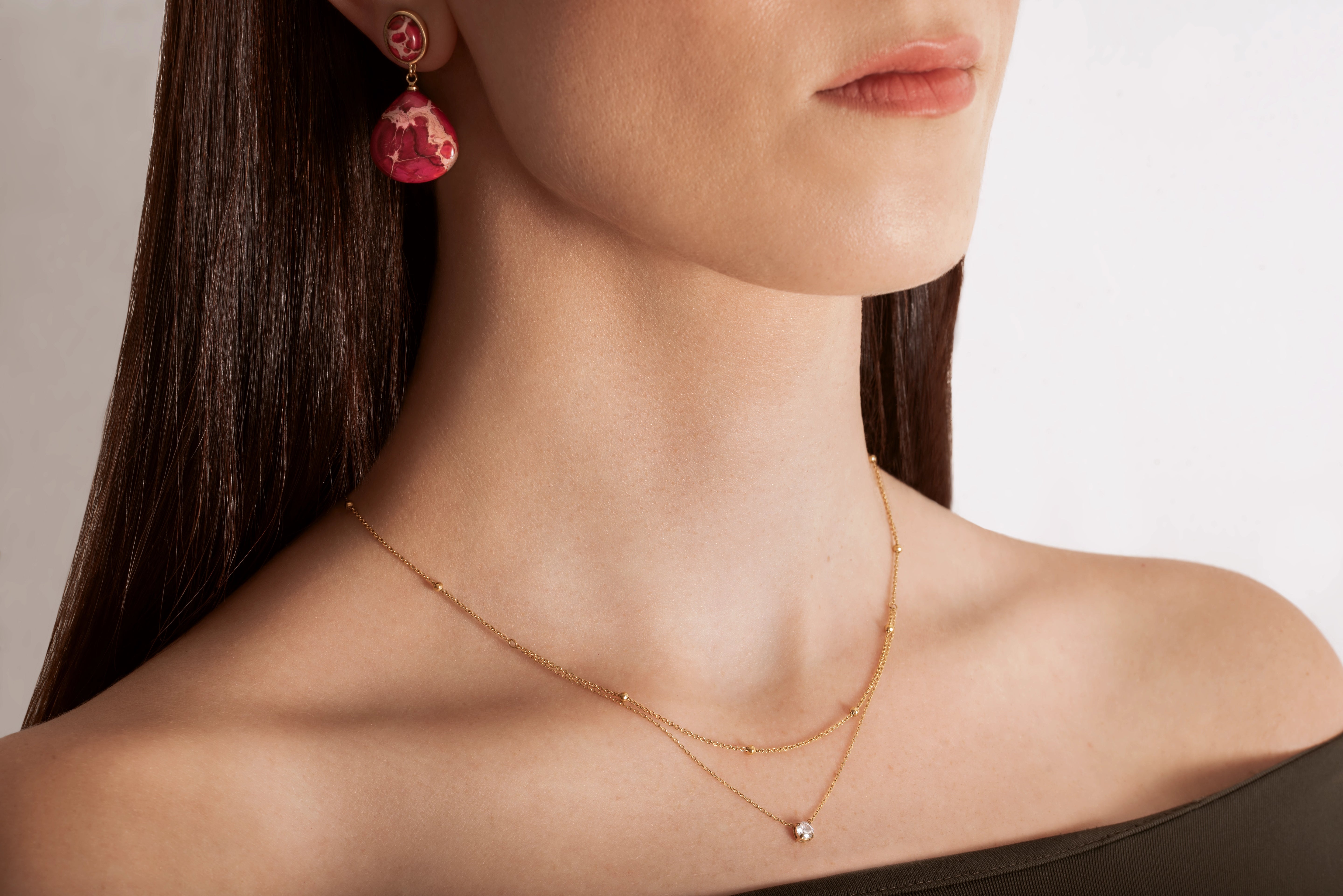 close up of a model wearing a gold-colored necklace with two layers, featuring tiny spheres on the upper strand and a crystal pendant on the lower chain