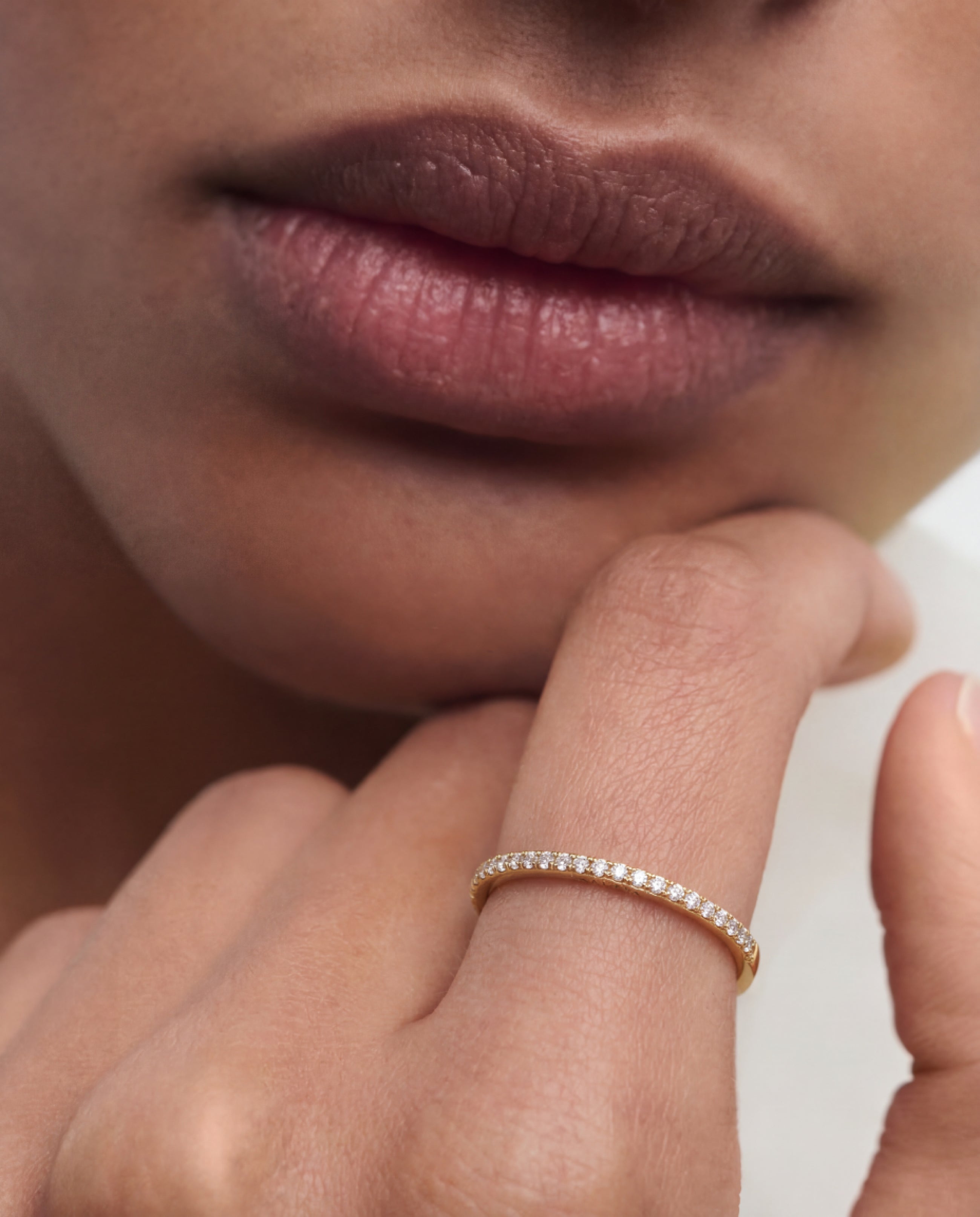 Close-up of a person's hand with a gold ring on a neutral background