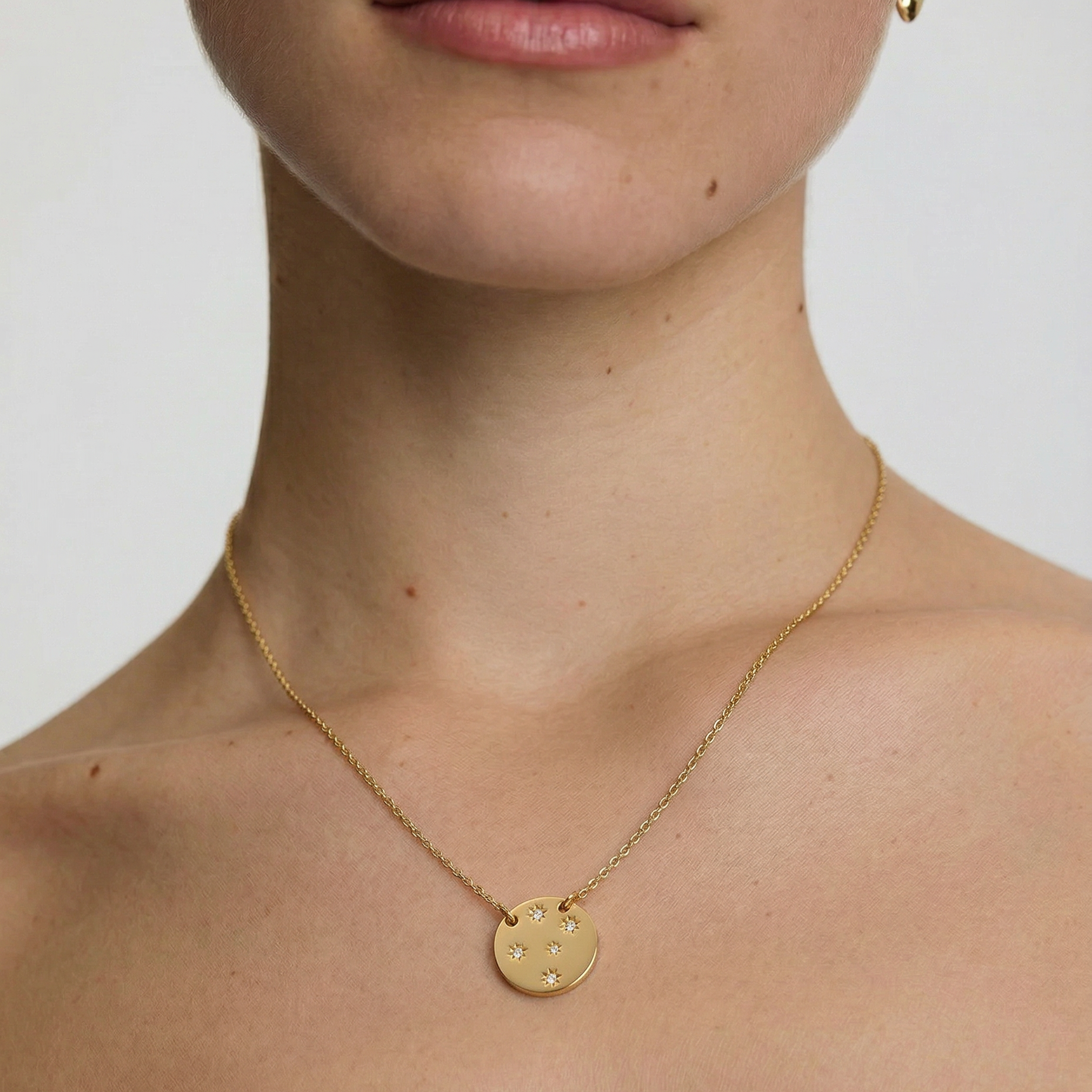 Gold necklace with a round pendant worn by a person on a plain background