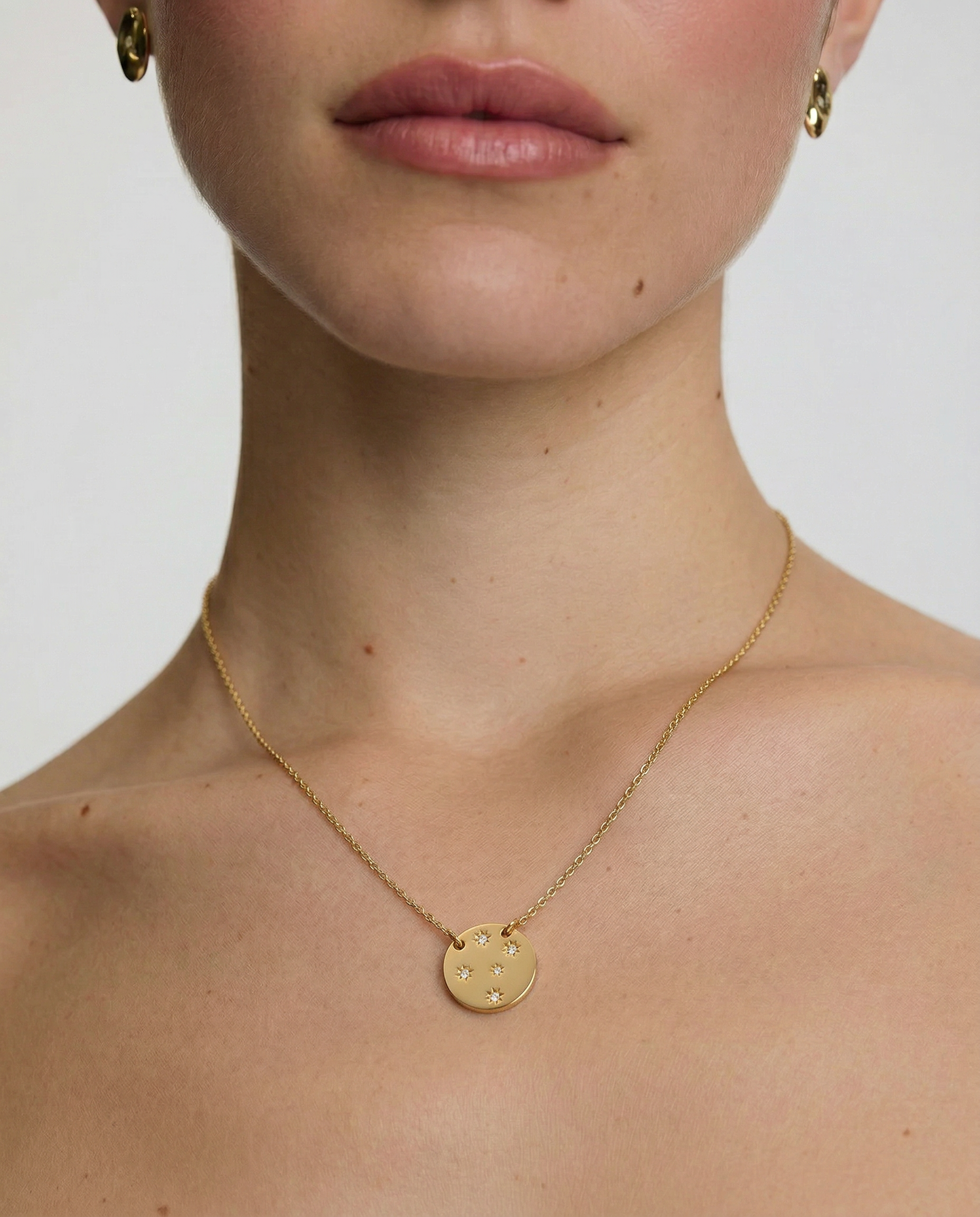 Gold necklace with a round pendant worn by a person on a plain background