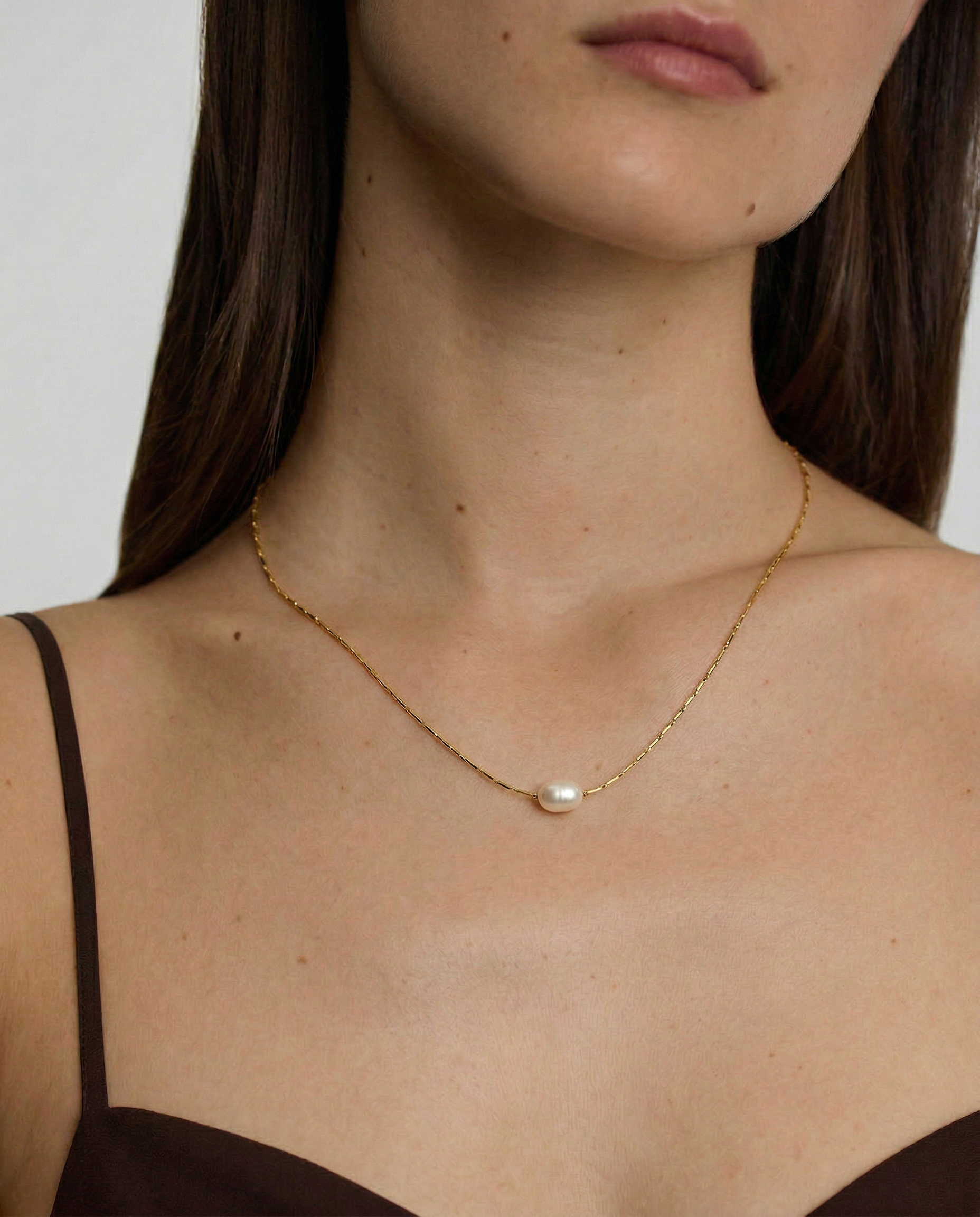 Woman wearing a delicate gold necklace with a pearl pendant against a neutral background