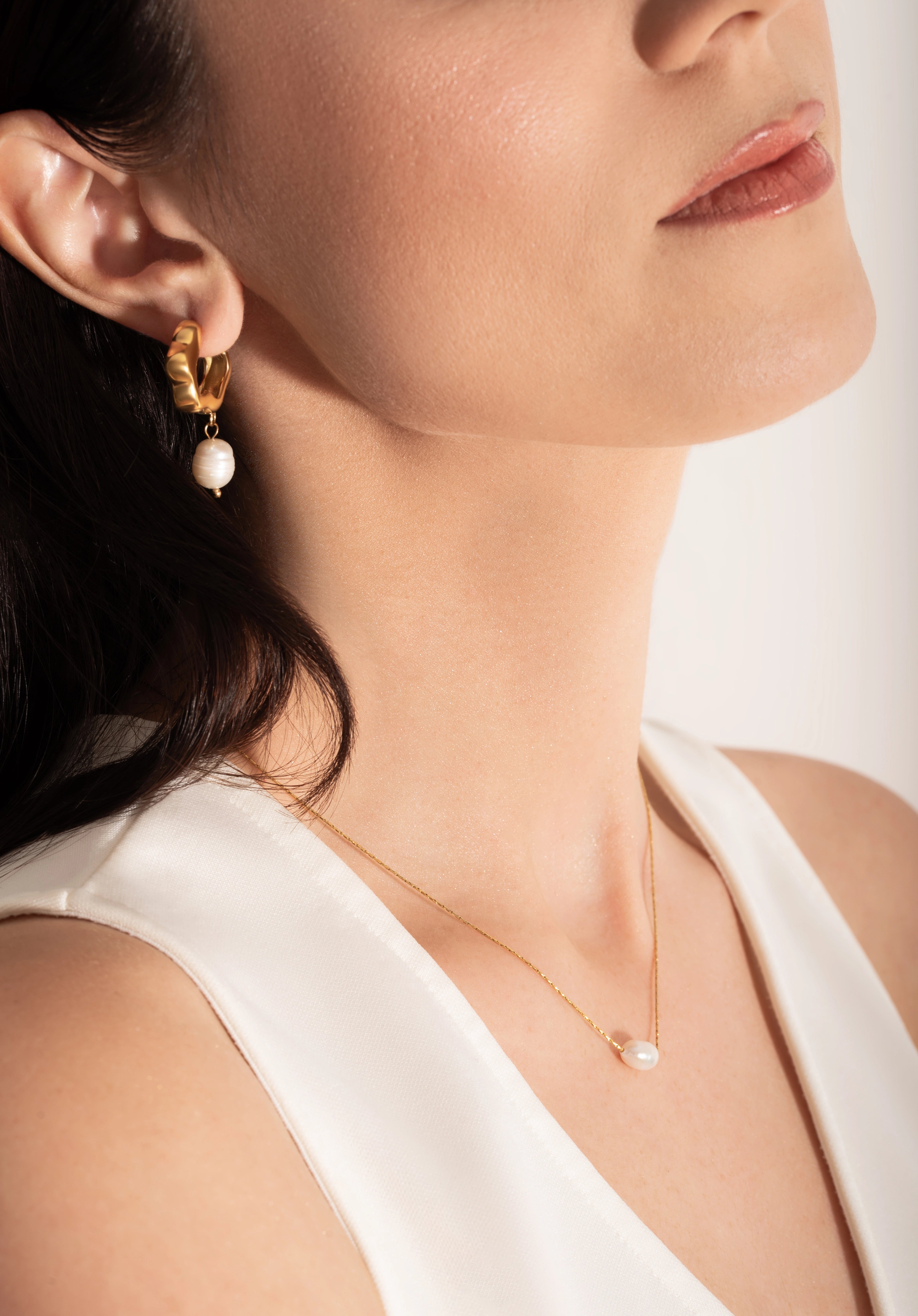 model wearing a  single white pearl pendant on a thin gold chain