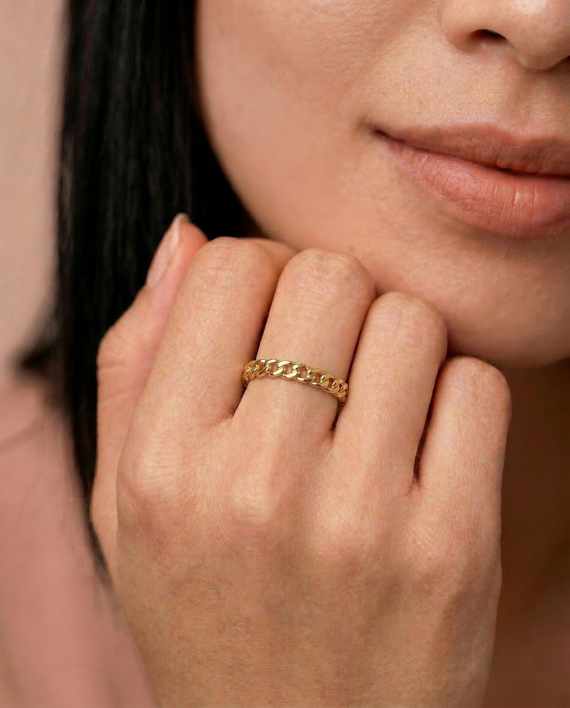 closeup of a model wearing a  gold-plated ring with a chain-inspired design, displaying a sleek, polished surface