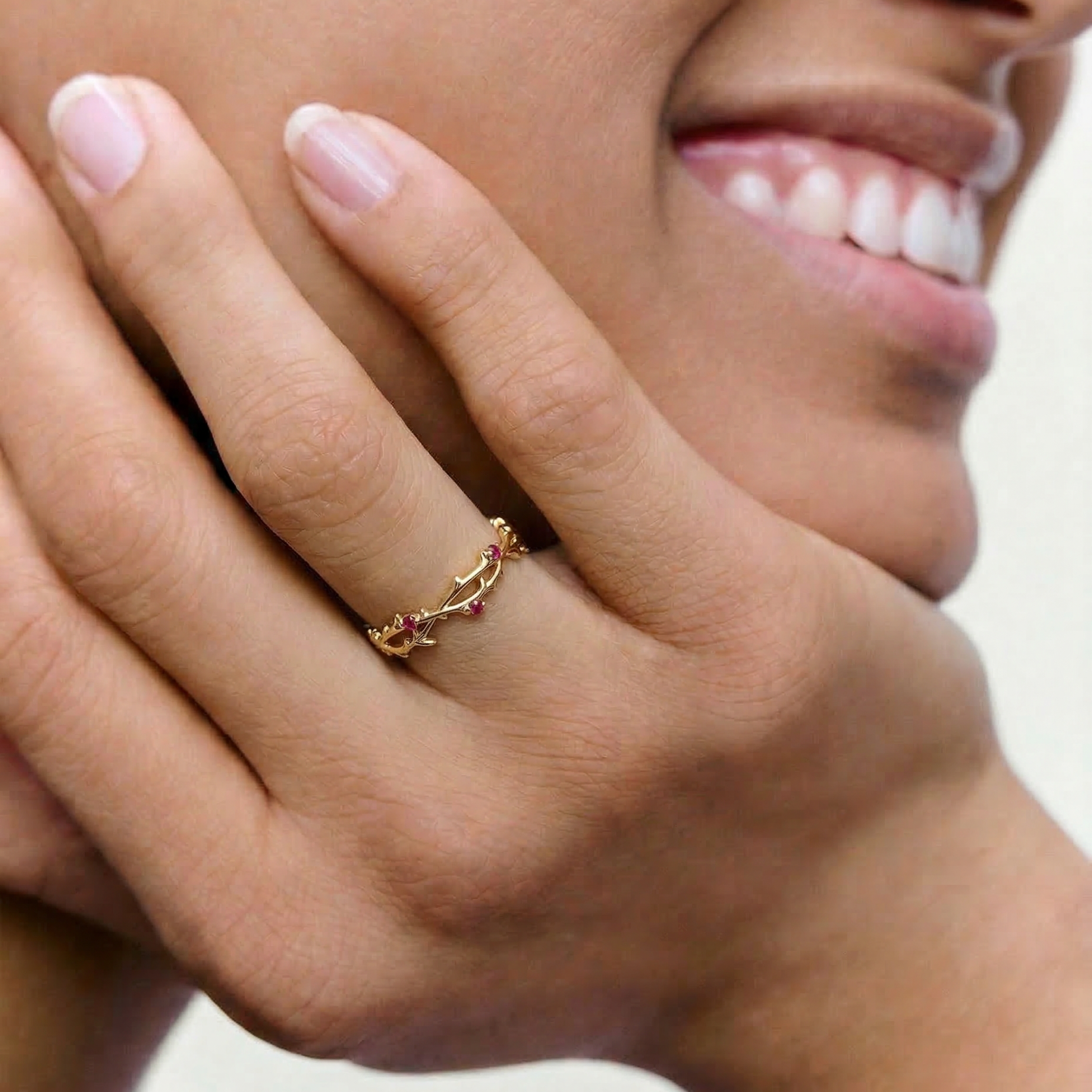 Close-up of a hand wearing a gold ring with gemstones, against a neutral background.
