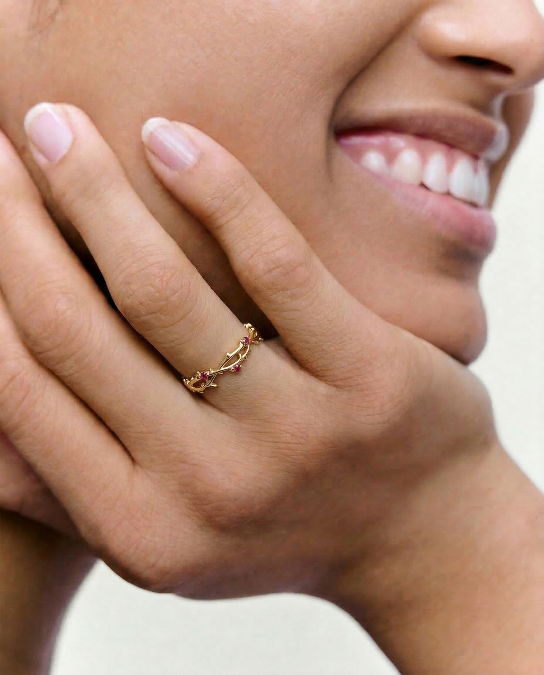 Close-up of a hand wearing a gold ring with gemstones, against a neutral background.