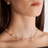 model wearing a colorful necklace with white freshwater pearls and multicolored beads, featuring a gold-colored chain and a heart charm.