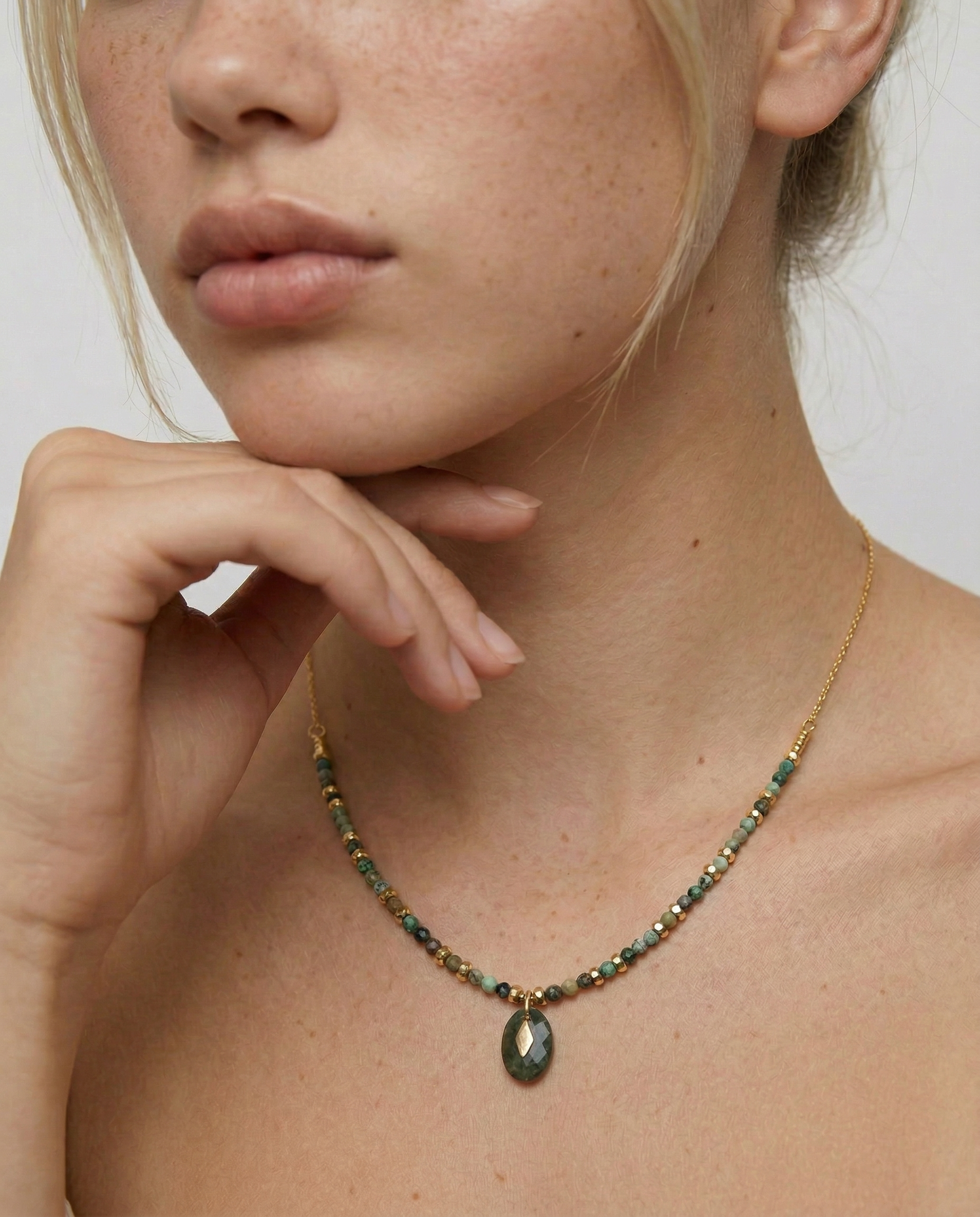 Close-up of a person wearing a gold-toned necklace with natural African turquoise beads in shades of sage, moss, and earth tones, featuring a smooth oval pendant.