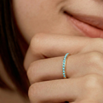 Close-up of a hand wearing a minimalist gold band with a partial pavé of turquoise stones 